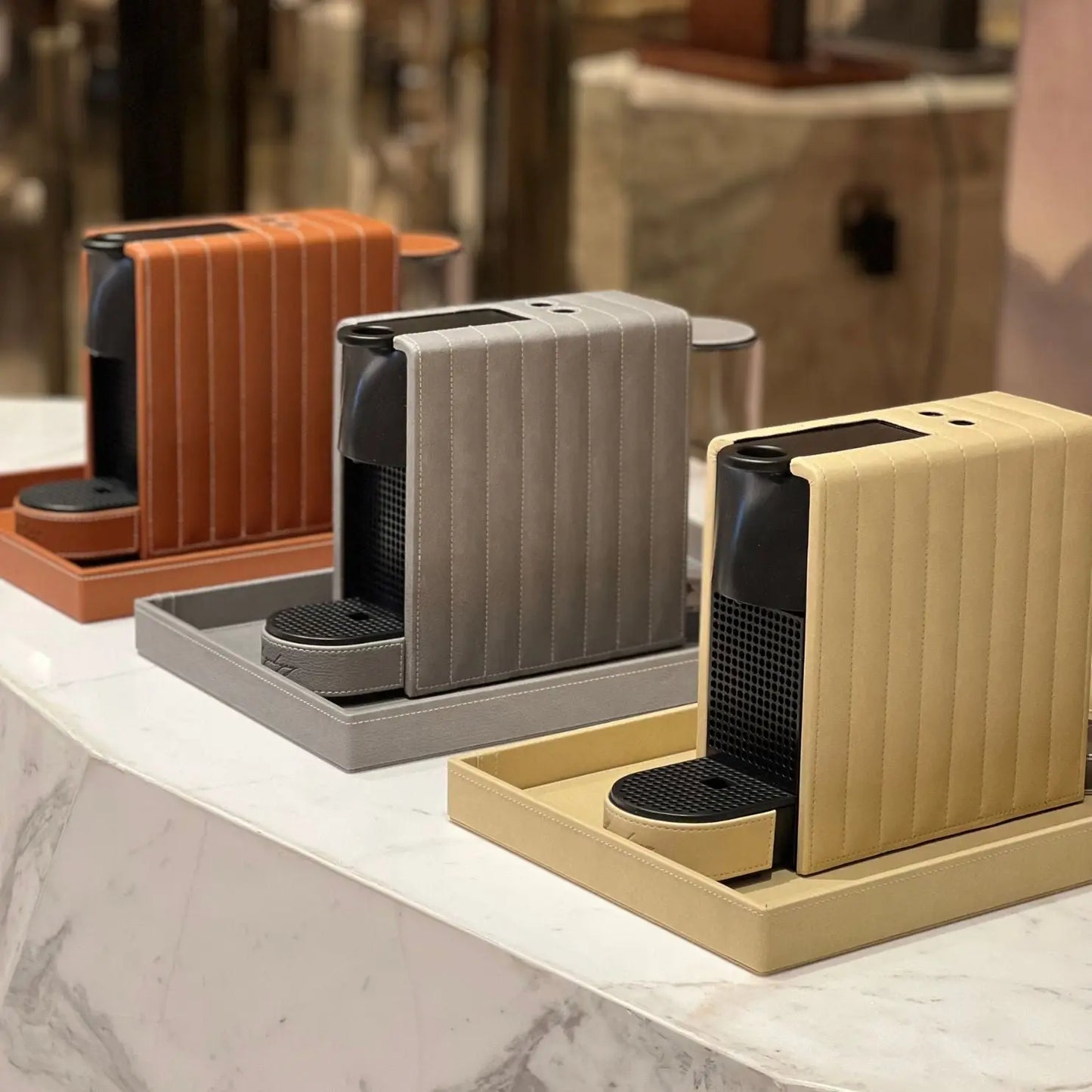 A trio of Nespresso Essenza Mini coffee machines featuring a stylish vegan leather covering, perfect for small spaces.