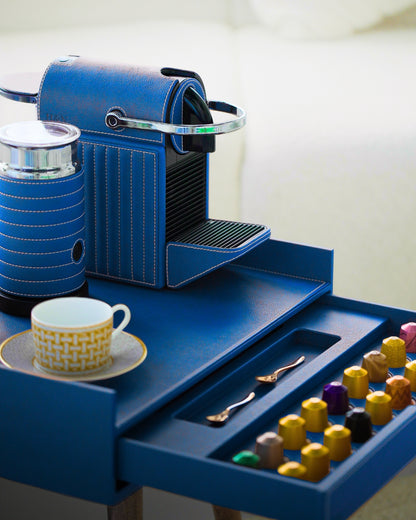 Blue luxury nespresso coffee machine wrapped in vegan leather with a drawer containing coffee pods and a cup on a saucer.