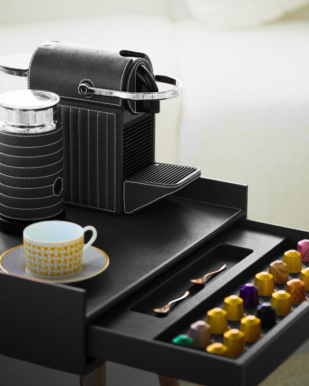 Black coffee machine with a drawer containing coffee pods and a cup on a saucer.