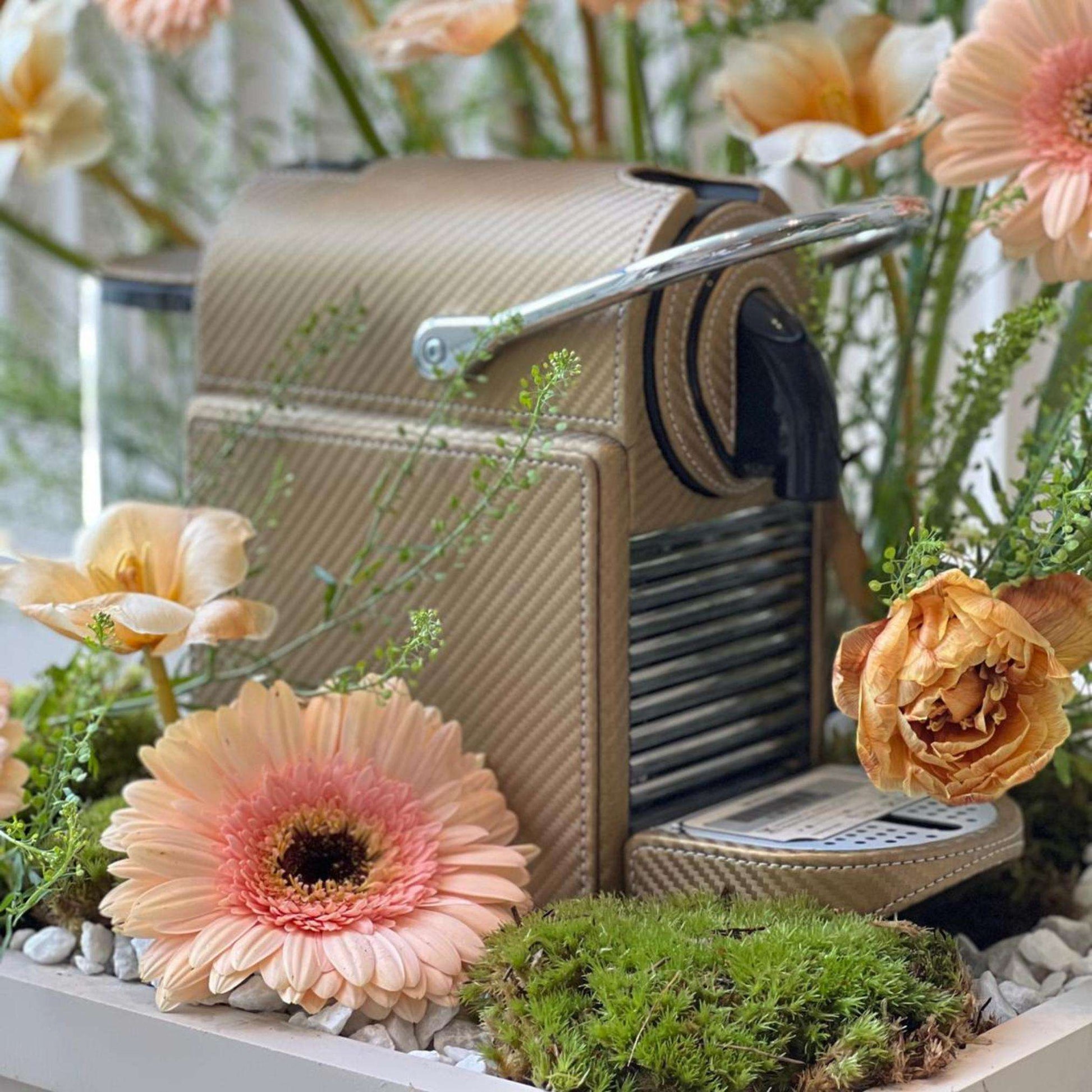 Golden Metallic Nespresso Pixie coffee machine covered in leather, styled as a gift with a floral arrangement