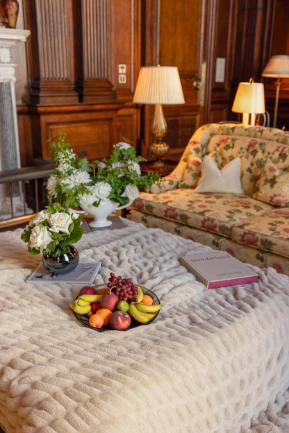 Living room with floral sofa, fruit plate, and decorative pillows on top of a fluffy creamy colored throw blanket