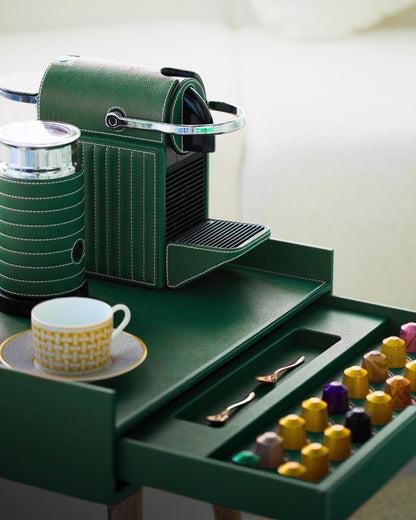 Green coffee machine with a drawer containing coffee pods and a cup on a white background